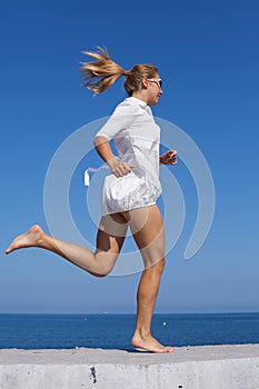 Barefoot girl in white short dress running along breakwater