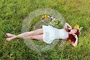 Barefoot girl in wreath lies on grass