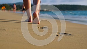 Barefoot lady walks along empty ocean beach under blue sky