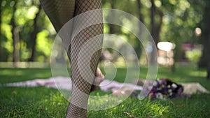 Barefoot legs of drunken woman in fishnet stockings walking to wine bottle taking alcohol drinking in sunny summer park