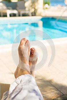 Barefoot male tourist relaxing by the outdoor swimming pool in seaside resort on sunny summer day