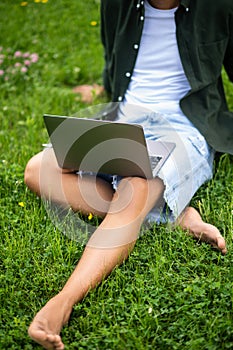 Barefoot man on grass with laptop without face