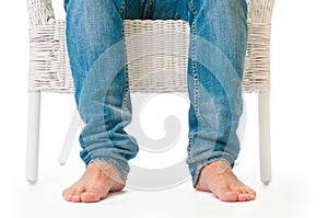 Barefoot man sitting in wicker armchair on white background