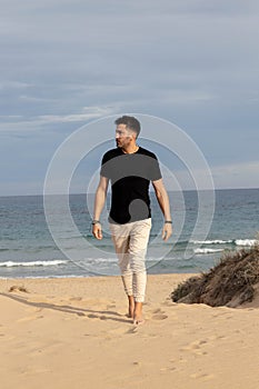 Barefoot man walking on the beach wearing casual