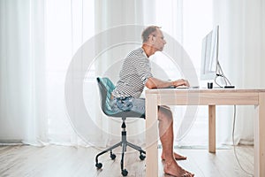 Barefoot Middle-aged writer man on a swivel chair typing down a text using the modern PC keyboard in the home living room. photo