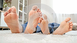 Barefoot parent with son lying on floor at home and moving feet