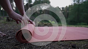 Barefoot person outspreading yoga mat on ground in pine forest.