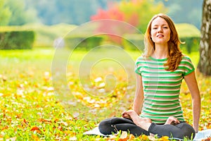 Barefoot red-haired girl practicing yoga in the park