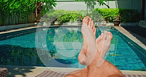 Barefoot relaxed man resting on lounger on holiday vacation near blue swimming pool water. Boy feet on the background