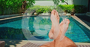 Barefoot relaxed man resting on lounger on holiday vacation near blue swimming pool water. Boy feet on the background