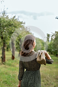 Barefoot serenity woman holding heels shoes in hand, walking on grass in nature, closeness to nature, sustainability, mindfulness