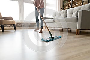 Barefoot woman cleaning floor with wet mop pad cropped image.