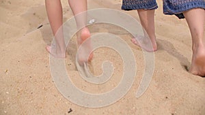 Barefoot woman and girl walking on sandy beach at sea. Back view barefoot women legs walking on sandy shore at summer