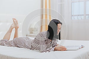 Barefoot young teenage girl lying on her bed reading a book or studying