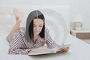 Barefoot young teenage girl lying on her bed reading a book or studying