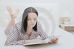 Barefoot young teenage girl lying on her bed reading a book or studying