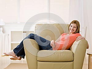 Barefoot young woman lounging on armchair at home