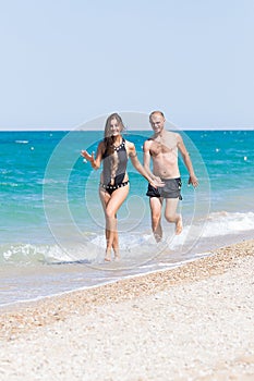 Barefoot young woman and man swimwear running along seashore