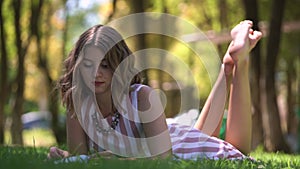 Barefoot young woman reads book lying on park lawn grass
