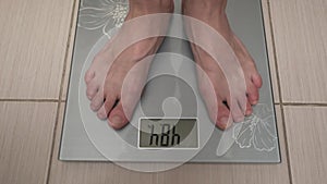 Barefoot young woman steps on electronic scales.