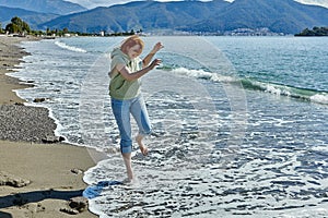 Barefoot young woman tries to walk on cool water in surf zone in early spring in Fethiye, Turkey.