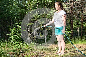 Barefoot young woman walks with a hose around the garden and waters the plants