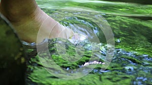 Barefooted boy cooling his feet in water with crystal clear water and idyllic floating creek in summertime shows outdoor hiking to