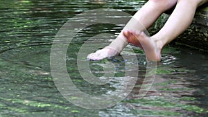 Barefooted boy cooling his feet in water with crystal clear water and idyllic floating creek in summertime shows outdoor hiking to