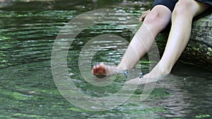 Barefooted boy cooling his feet in water with crystal clear water and idyllic floating creek in summertime shows outdoor hiking to
