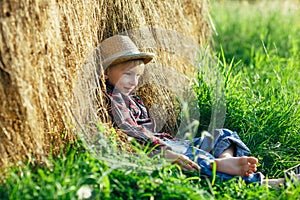 Barefooted boy in straw hat resting in haystack