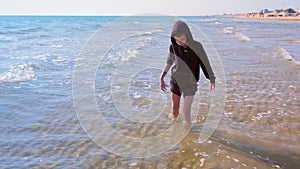 Barefooted child boy walks on the sand beach at sea cold water on vacation.