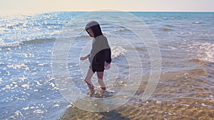 Barefooted child boy walks on the sand beach at sea water on vacation.