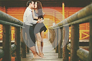 Barefooted love - couple kisses ardently on the wooden bridge