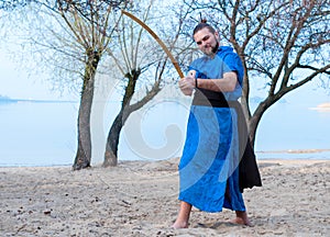 Barefooted man in blue kimono, bun and sticks on head training with sword