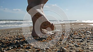 Barefooted woman tourist walks on sea shells on sand beach makes nature feet massage, side view. Girl traveller travel