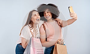 Bargainbuddies. Studio shot of two young women carrying a bunch of shopping bags and taking a selfie.