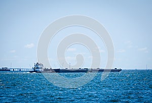 Barge being pushed by a tugboat in tropical blue ocean water.