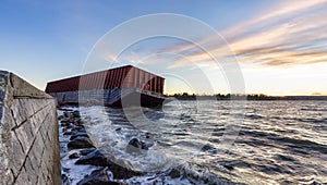 Barge container ship collided on a rocky coast during wind storm. Sunset Sky.