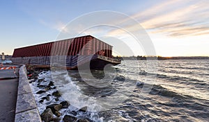 Barge container ship collided on a rocky coast during wind storm. Sunset Sky.