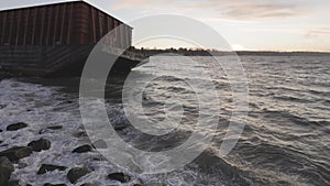 Barge container ship collided on a rocky coast during wind storm. Sunset Sky.