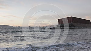 Barge container ship collided on a rocky coast during wind storm. Sunset Sky.