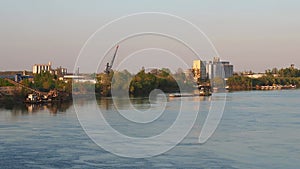 The barge departs from the river bank with an industrial zone. Water flow on the Sava river, Serbia, Sremska Mitrovica