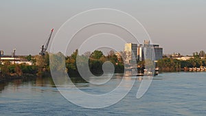 The barge departs from the river bank with an industrial zone. Water flow on the Sava river, Serbia, Sremska Mitrovica