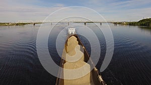 Barge loaded with sand and gravel floats on the wide river on the background of the bridge. Aerial view