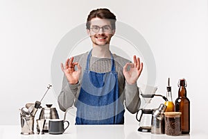 Barista, cafe worker and bartender concept. Portrait of satisfied, pleased young male employee in apron smiling assuring