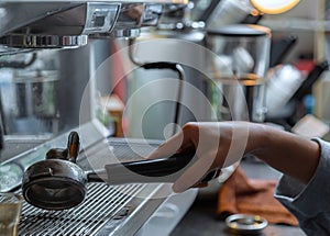 The barista is cleaning the tools. The barista is cleaning the coffee machine handle on the coffee console.