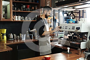 Barista frothing milk in metal pitcher with coffee machine steam wand