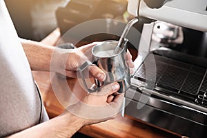 Barista frothing milk in metal pitcher with coffee machine wand at bar counter