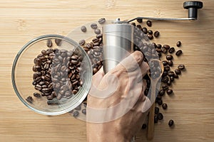 Barista hand holding a coffee grinders with coffee beans and glass bowl on table background