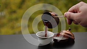 Barista hand pouring tasty hot coffee in cup brewed in traditional turkish pot, cafe table outdoors